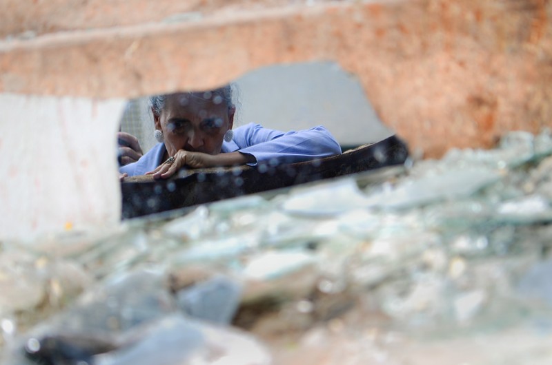 Pedaço de espelho quebrado reflete a imagem de Tactiana recolhendo destroços sobre uma caçamba - Pedro França/Agência Senado